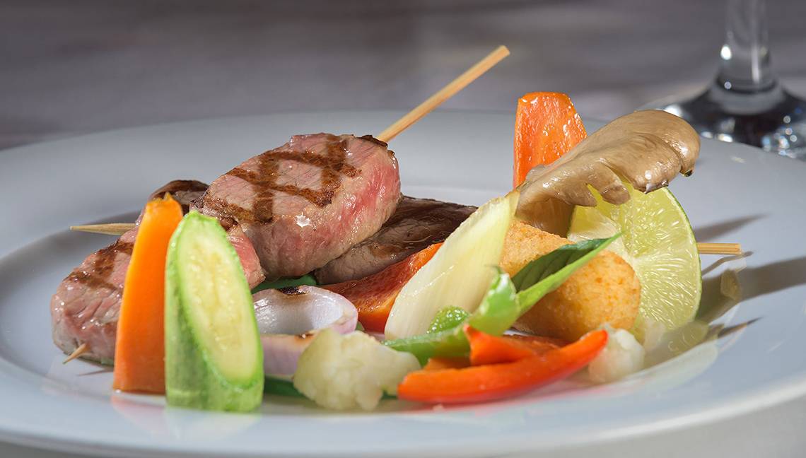 Gegrillter Fleischspieß mit Gemüse auf einem weißen Teller, serviert im Atrium Palace Thalasso Spa Resort & Villas.