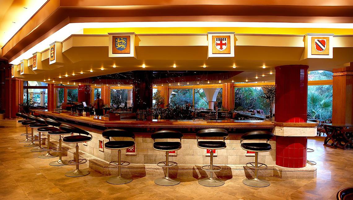 Innenansicht der Bar des Atrium Palace Thalasso Spa Resort & Villas mit Barhockern und einer Theke.