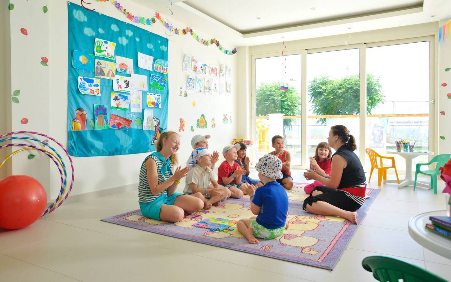 Gruppe von Kindern und zwei Erzieherinnen, die eine Runde sitzen und singen, im Pernera Beach Hotel.