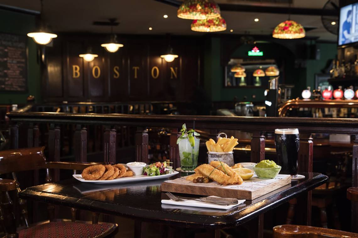 Boston Pub Tisch mit Essen und Getränken, darunter Pommes und Salat.