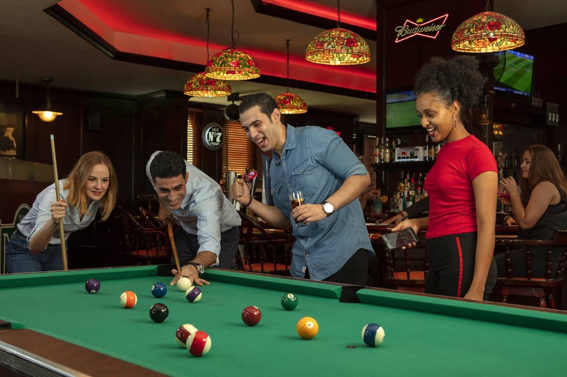 Im Hotel Jumeira Rotana spielen Gäste Billard in einer Bar mit bunten Lichtern und Fernsehern.