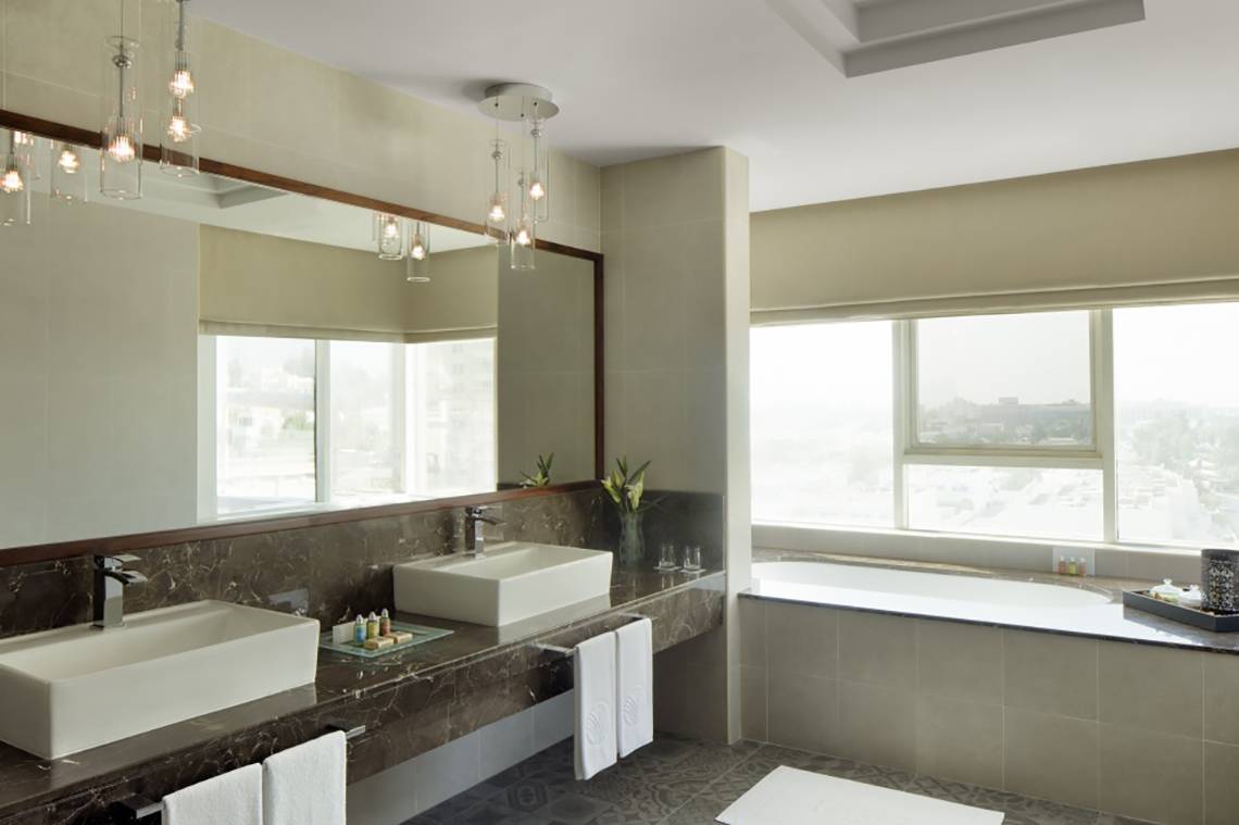 Badezimmer im Jumeira Rotana Hotel mit zwei Waschbecken, Badewanne und Fenstern.