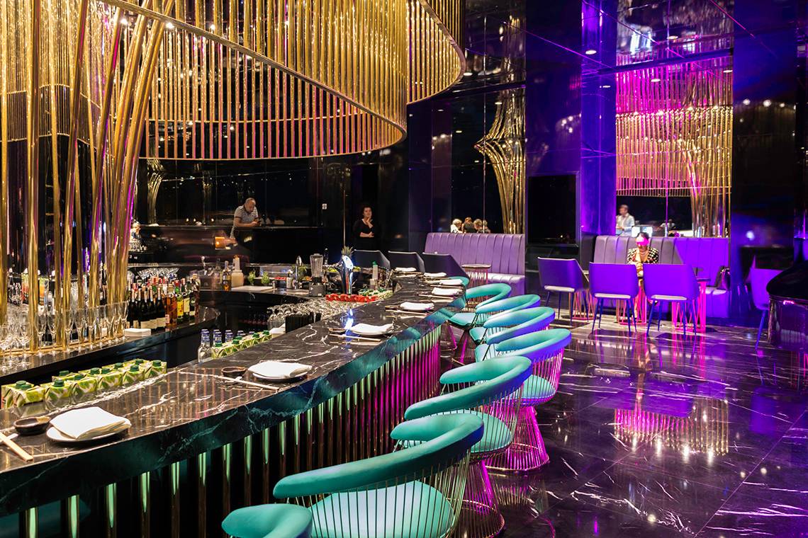 Bar im Land of Legends Kingdom Hotel mit goldenen Kronleuchtern und blauen Stühlen.