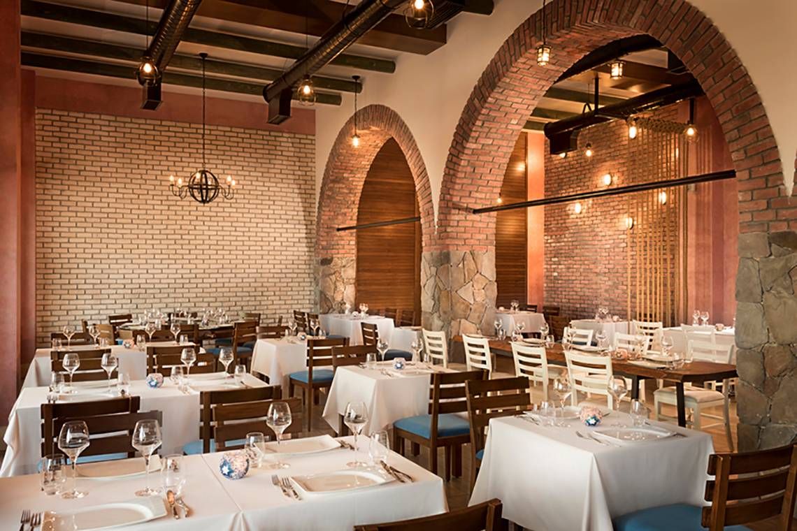 Innenansicht des Restaurants im Rixos Bab Al Bahr Hotel mit runden Bögen und Steinwänden.