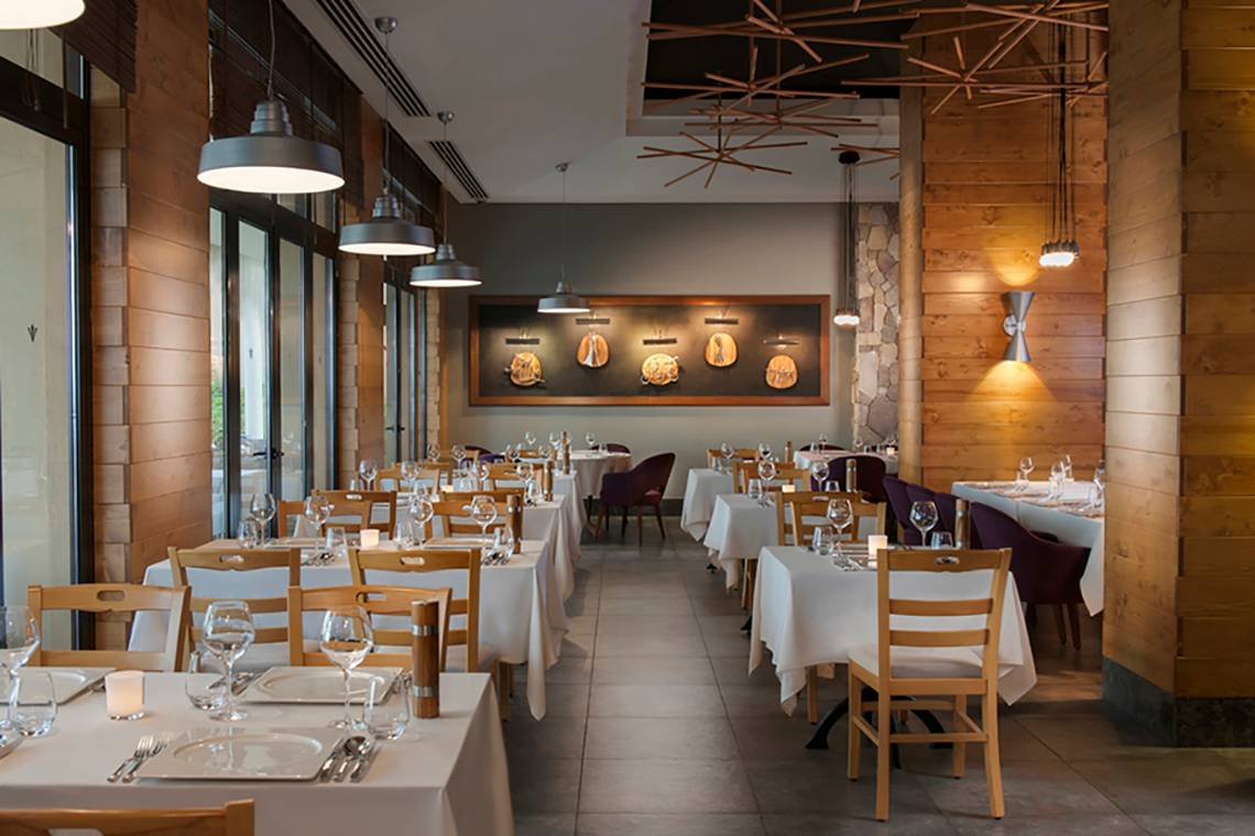 Innenansicht des Rixos Bab Al Bahr Restaurants mit Tisch und Stühlen, Holzwänden und Kronleuchtern.