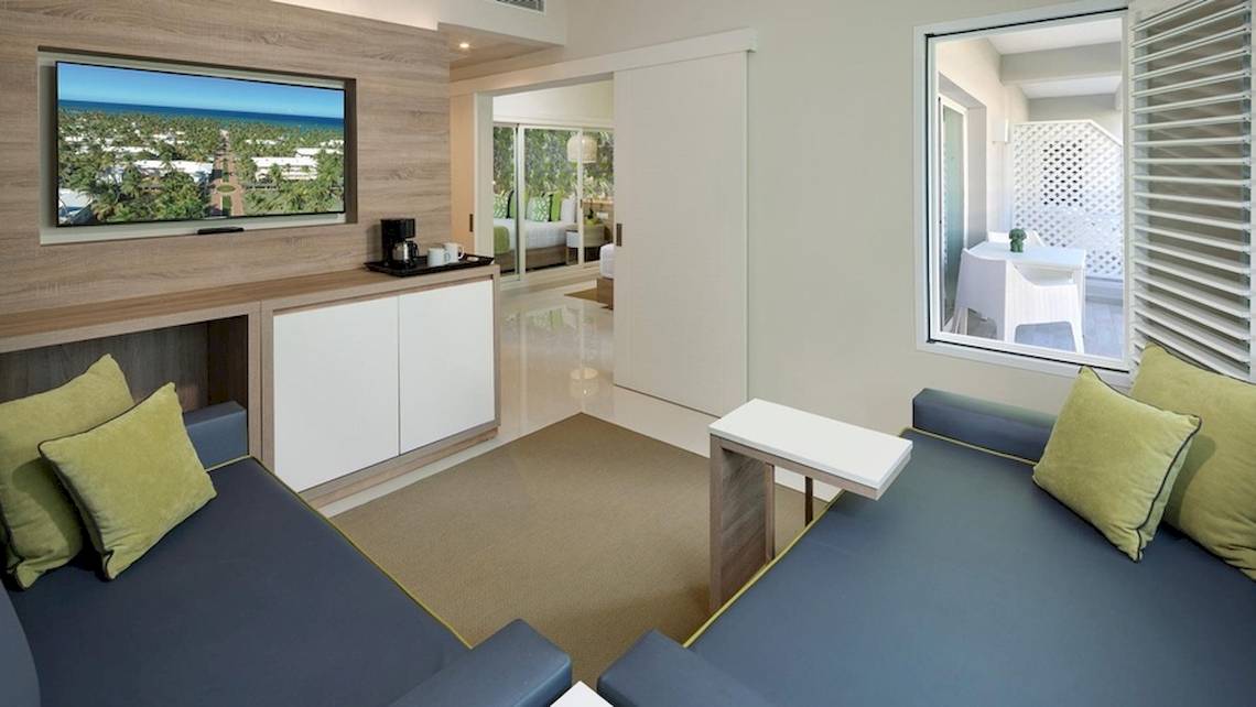 Wohnzimmer des Grand Sirenis Punta Cana Resort mit zwei blauen Sofas, Fernseher und Tisch