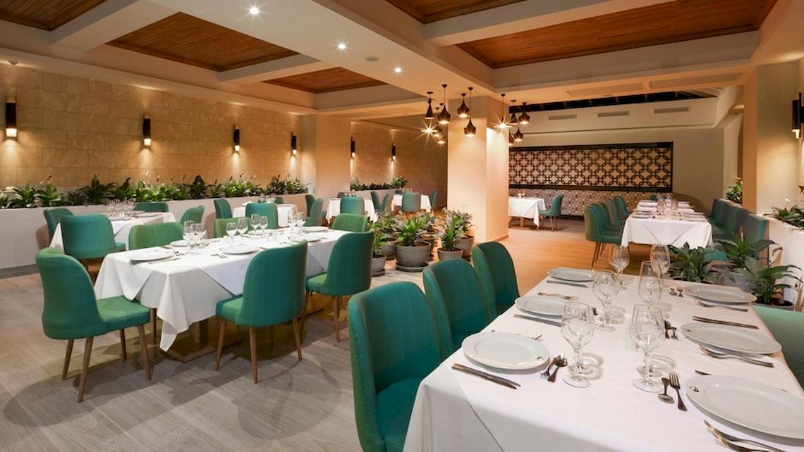 Das Grand Sirenis Punta Cana Resort verfügt über ein elegantes Restaurant mit grünen Stühlen und weißen Tischdecken.