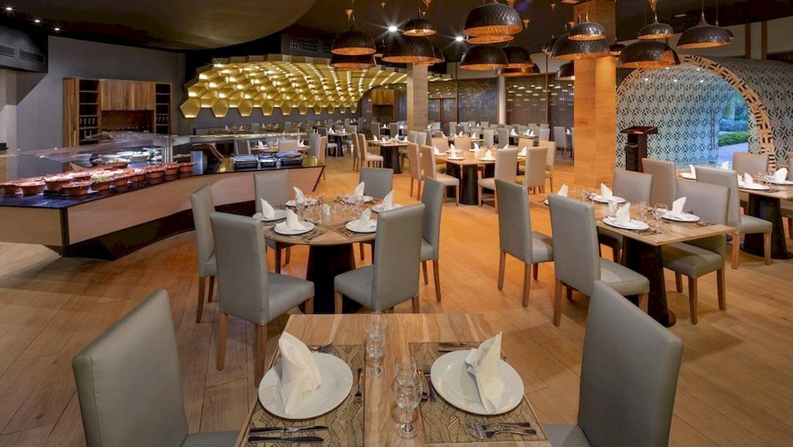 Innenansicht des Restaurants im Grand Sirenis Punta Cana Resort mit hölzernen Tischen und Stühlen.