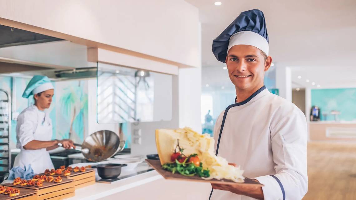 Ein Koch im Iberostar Waves Alcudia Park Hotel präsentiert ein Gericht in der Küche.