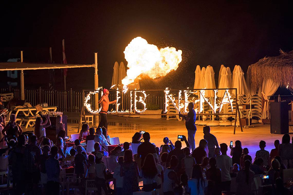 Feuershow mit Schriftzug Club Nena bei Nacht im Freien vor einer tanzenden Menge.