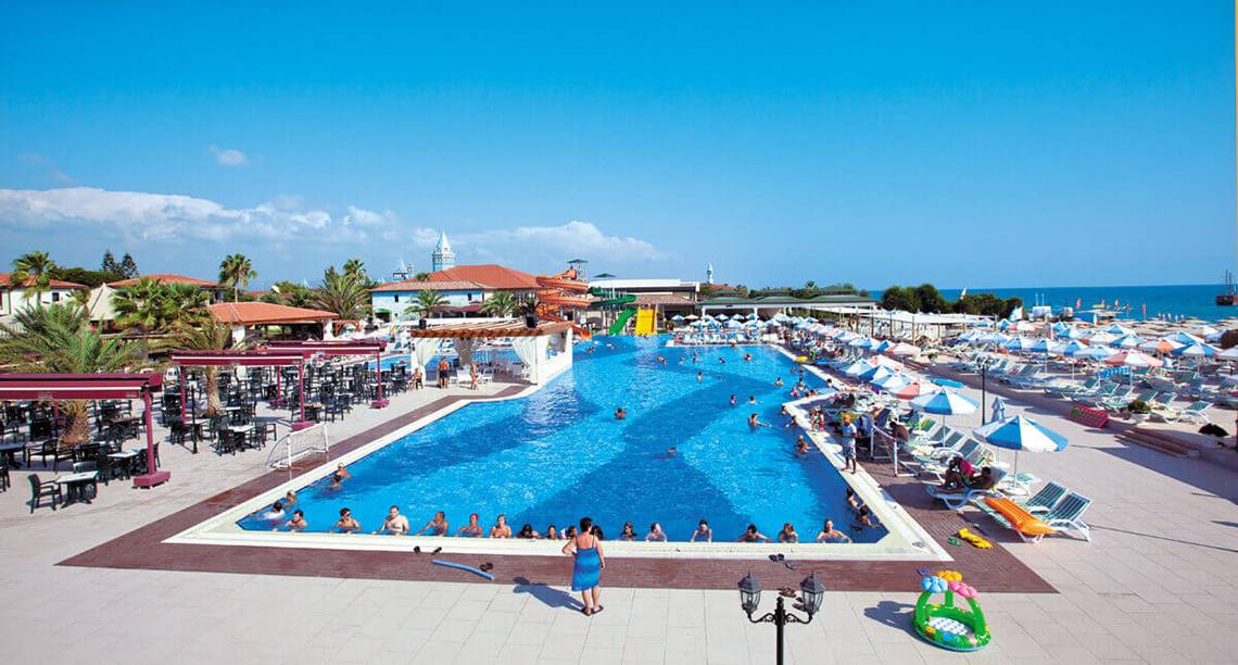 Aussicht auf den Swimmingpool des Club Nena Hotels mit vielen Gästen und Sonnenschirmen.