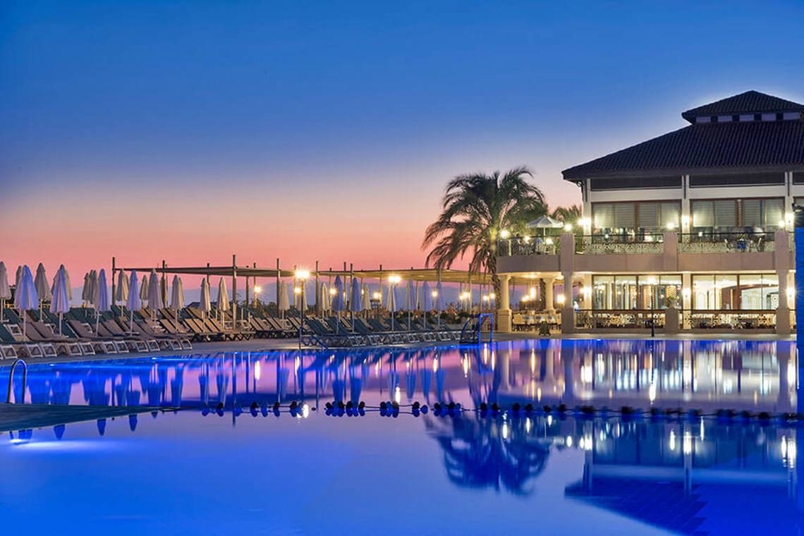 Pool im Club Nena Hotel bei Einbruch der Dunkelheit, beleuchtet und reflektiert im Wasser.
