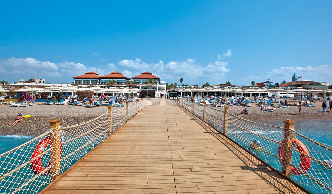 Club Nena Hotel am Strand mit vielen Gästen, Liegestühlen und Schirmen.
