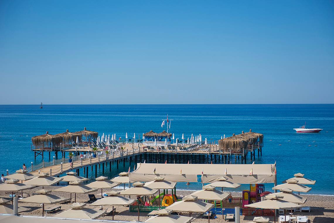 Aussicht auf das Club Nena Hotel am Meer mit Pier, Sonnenschirmen und Spielen am Strand.