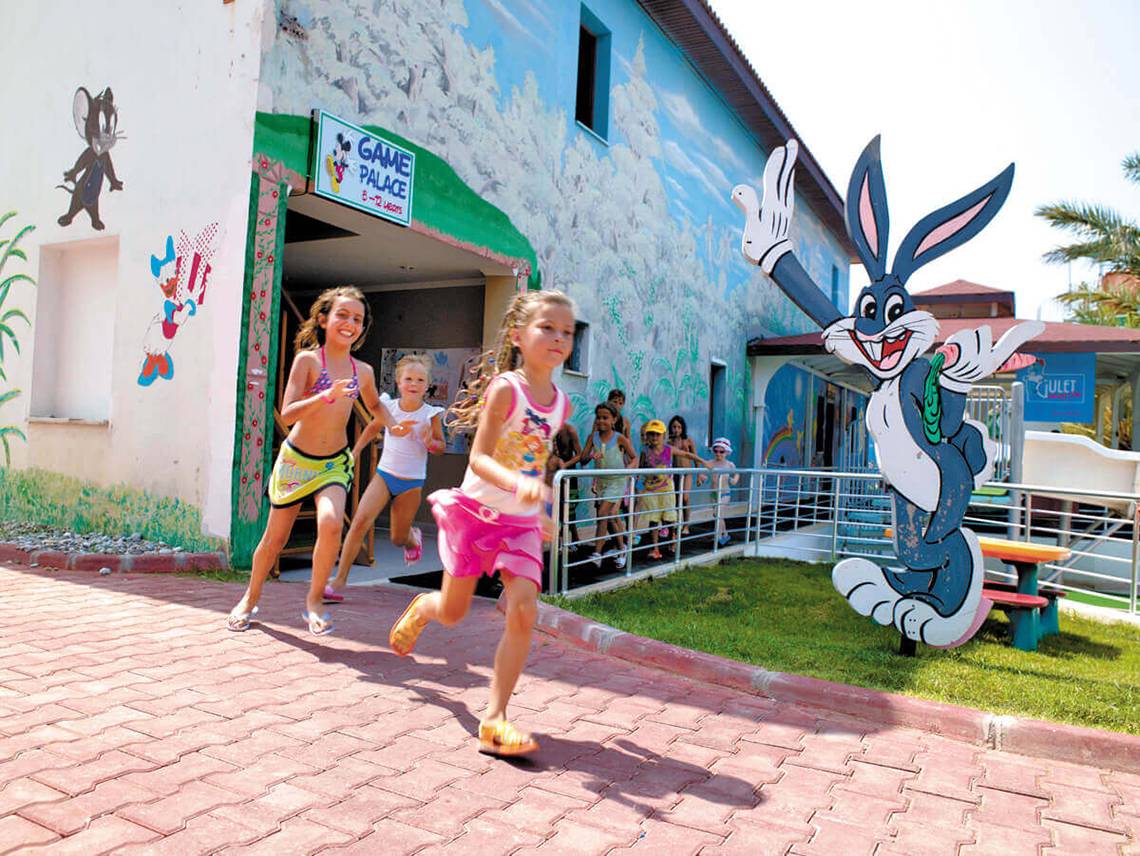 Kinder laufen vor dem Club Nena Hotel, das mit farbenfrohen Wandmalereien und einer riesigen Bugs Bunny Figur dekoriert ist.
