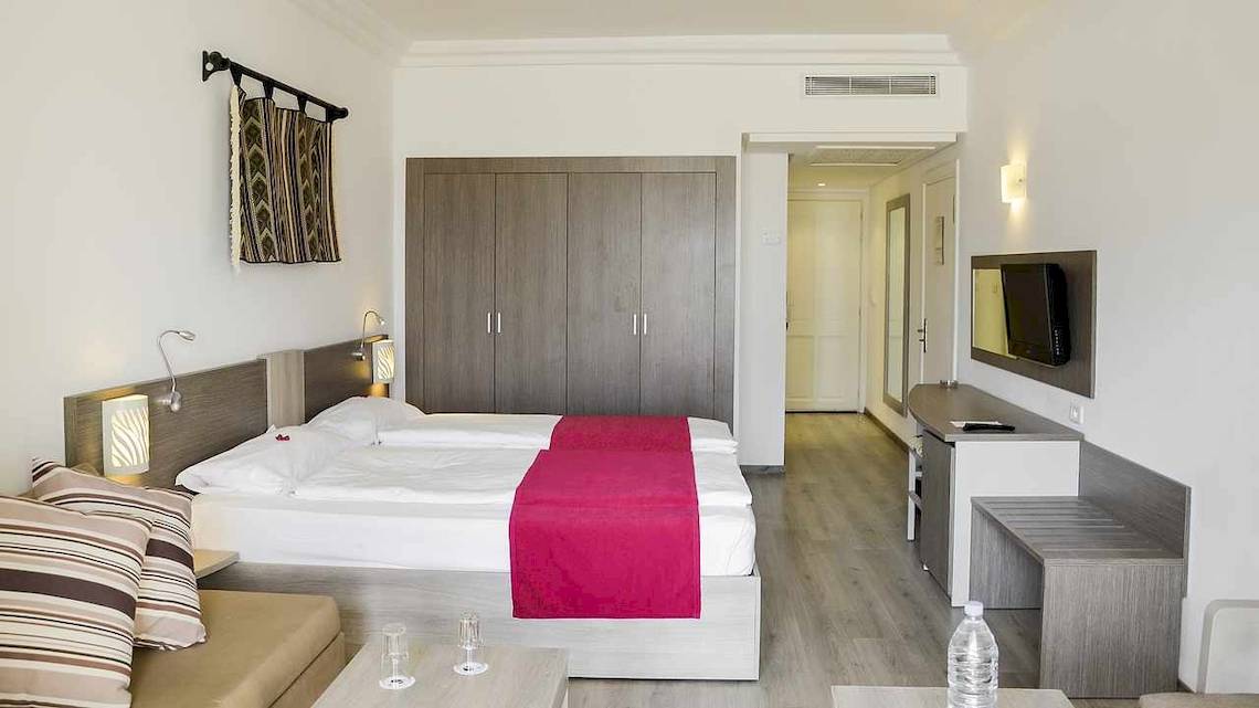 Ein modernes Hotelzimmer im Robinson Djerba Bahiya mit Doppelbett, Nachttischen, Fernseher und Kleiderschrank.