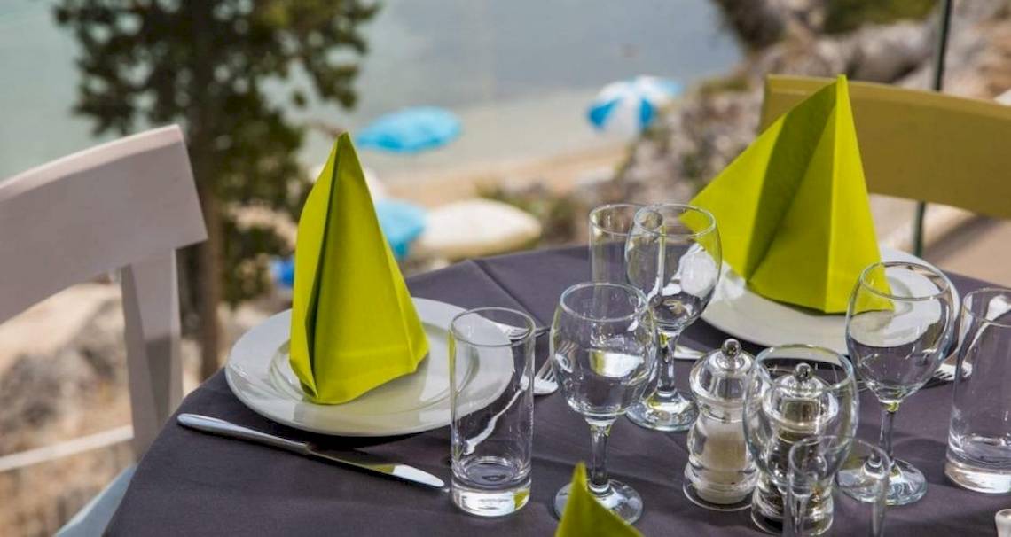 Ein Tisch auf der Terrasse des Osmine Slano Hotels mit grünen Servietten und Gläsern.