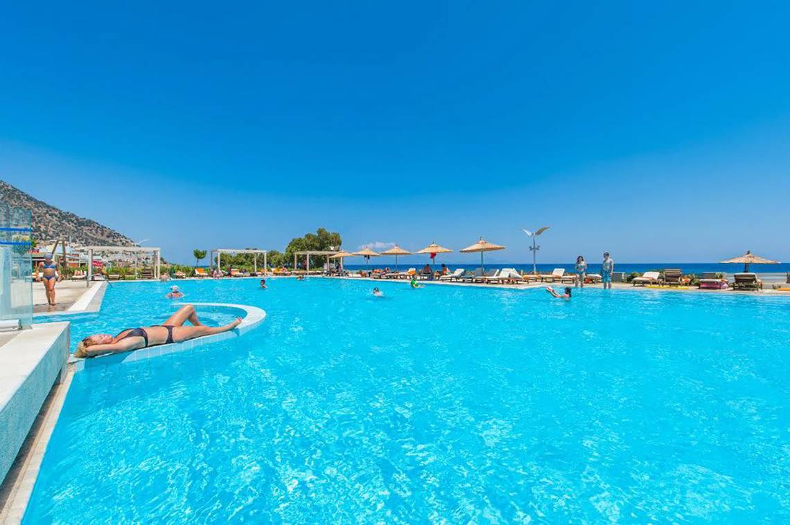 Ein Schwimmbad im Freien am Strand mit vielen Gästen, die in Akti Palace Hotel entspannen.