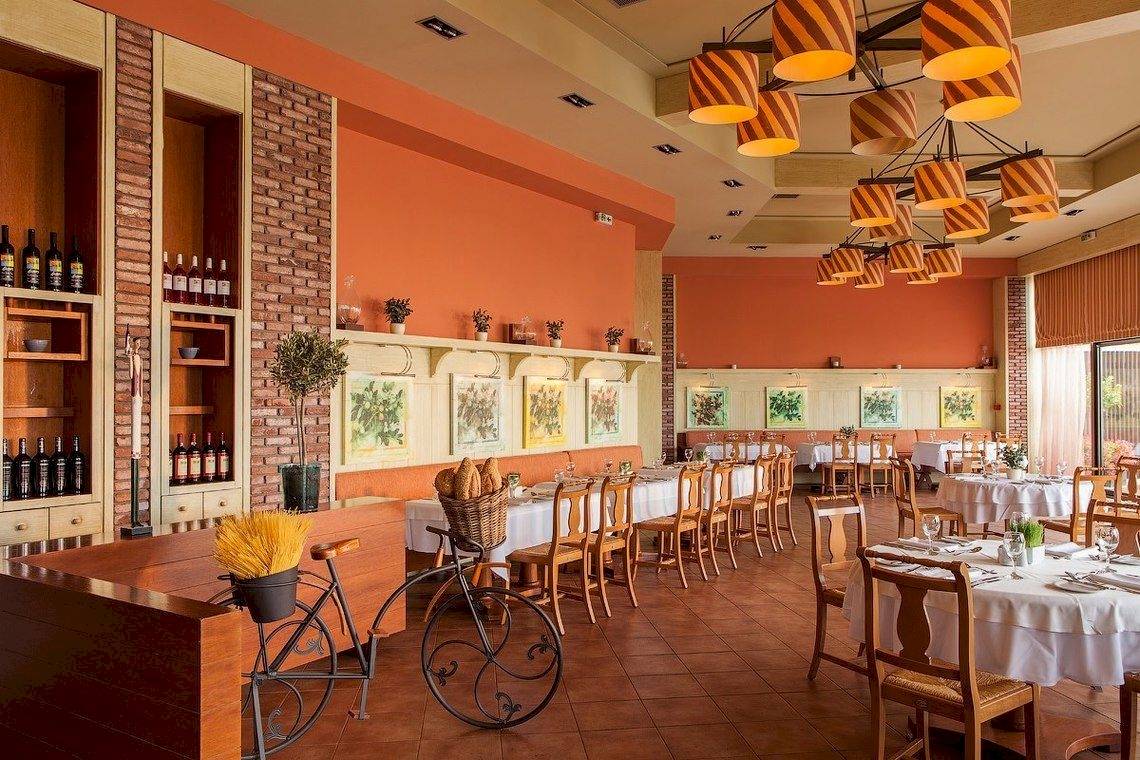 Innenansicht des Ikos Oceania Restaurants mit gedeckten Tischen, Holzstühlen und einer alten Fahrraddekoration.