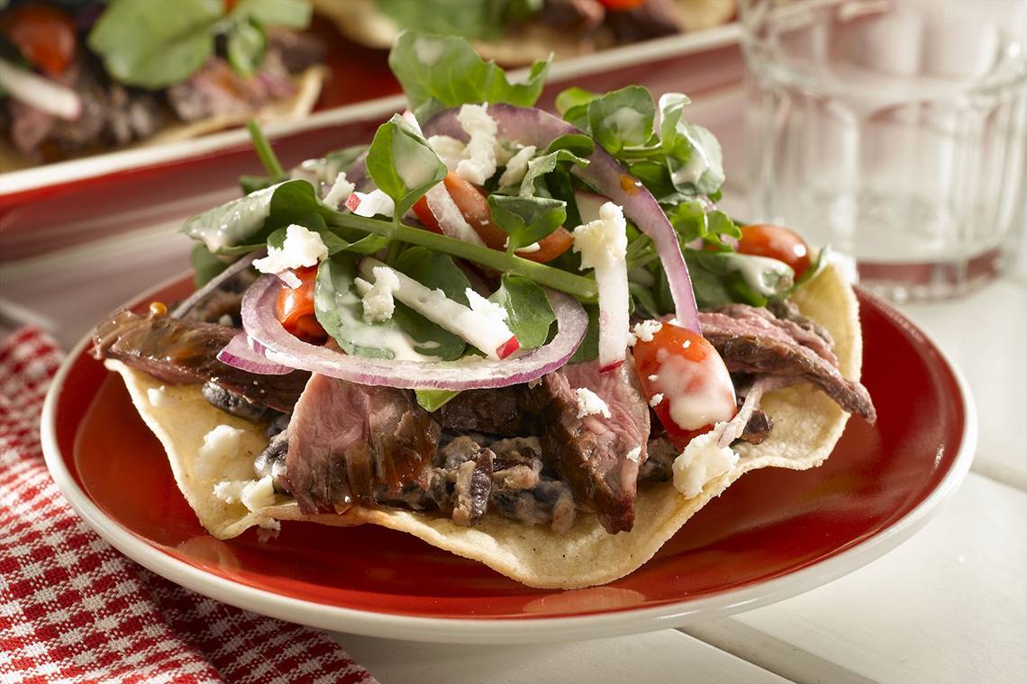 Ein Fleisch-Taco mit Gemüse auf einem roten Teller, serviert mit einem Glas Wasser.