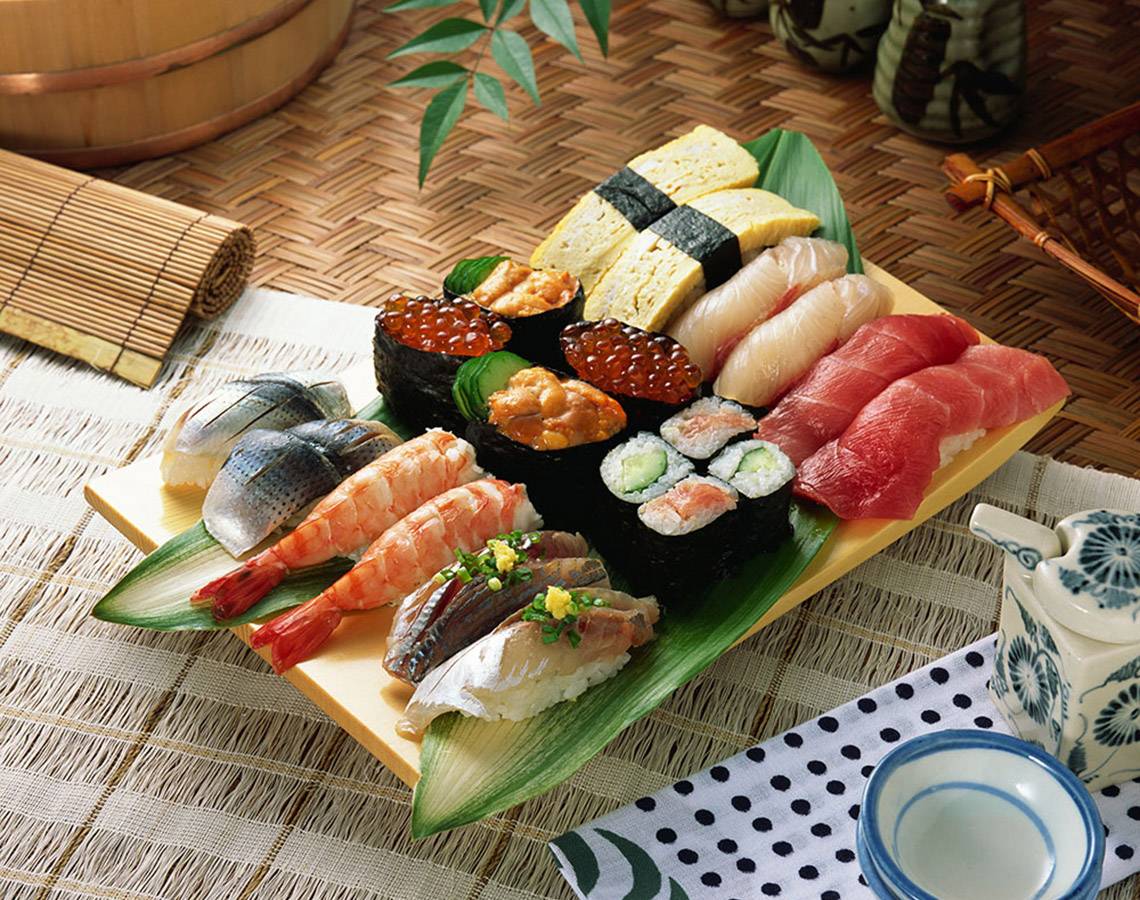 Eine Vielzahl von Sushi auf einem gelben Teller, der auf einem grünen Palmblatt liegt.