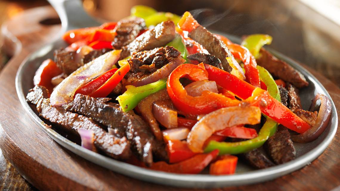 Eine Platte mit Fajitas, bestehend aus Fleisch, Paprika und Zwiebeln, serviert auf einem runden Teller.