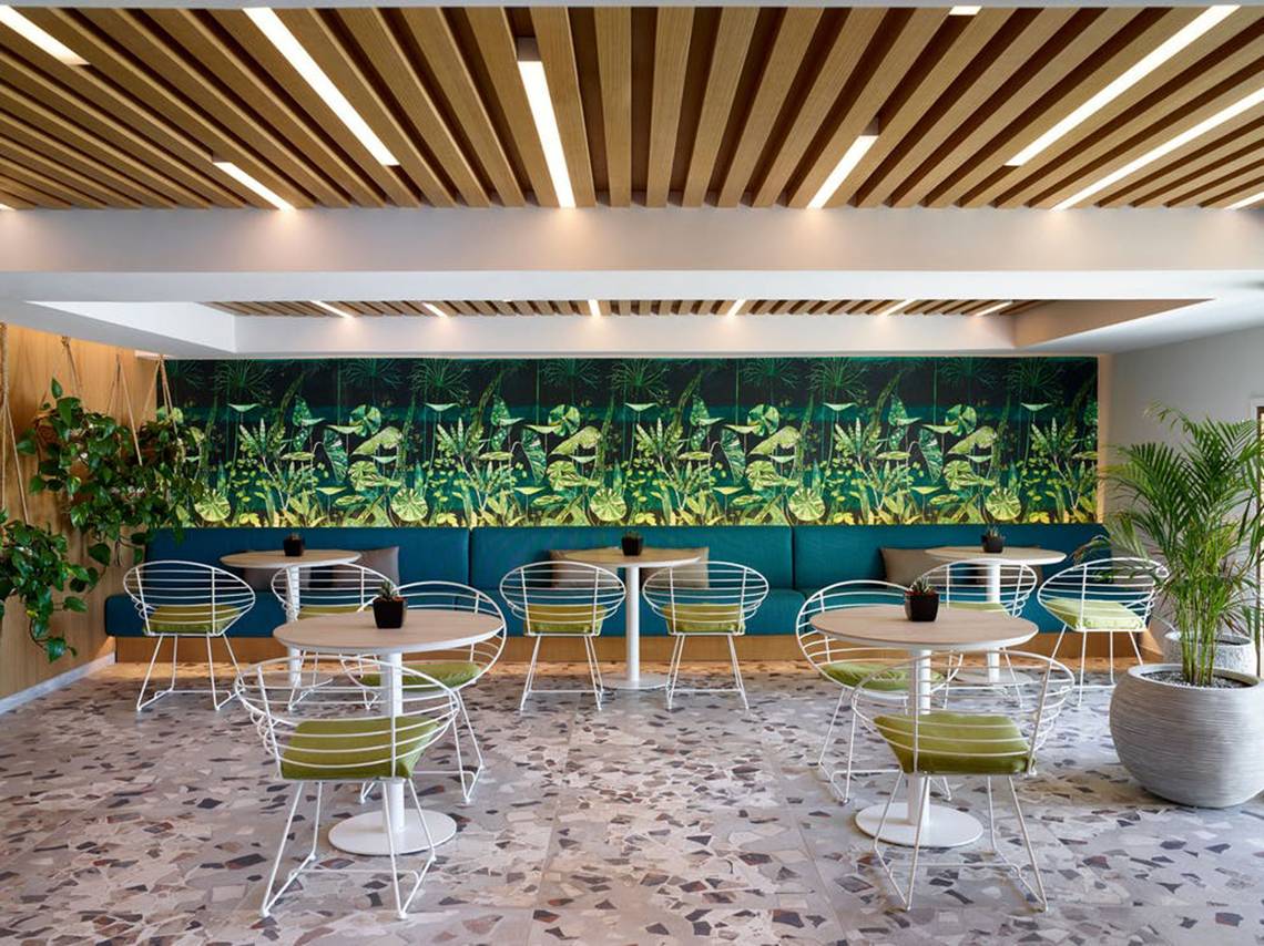 Innenraum der Lounge im Rhodes Bay Hotel & Spa mit grüner Wandmalerei und weißen Tischen.