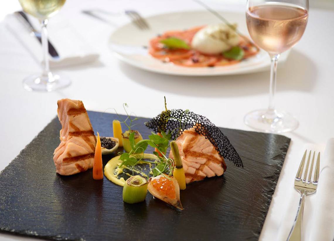 Feine Speisen auf einem Tisch im Rhodes Bay Hotel & Spa mit gebratenem Lachs, Gemüse und Getränken.