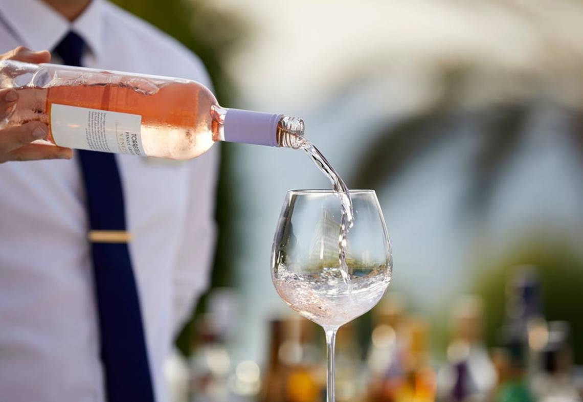 Mitarbeiter des Rhodes Bay Hotel & Spa gießt rosa Wein in ein Glas