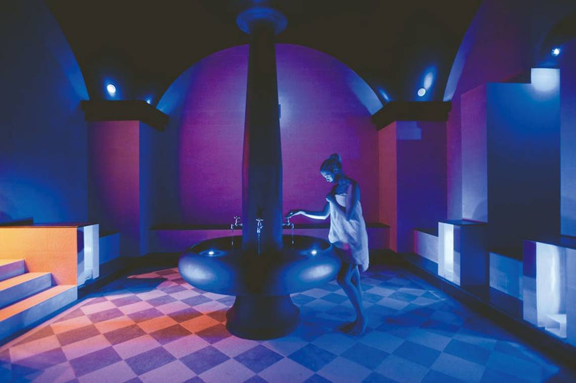 Eine Frau steht in einem Badezimmer des Rhodes Bay Hotel & Spa, das mit blauen und lilafarbenen Lichtern dekoriert ist.