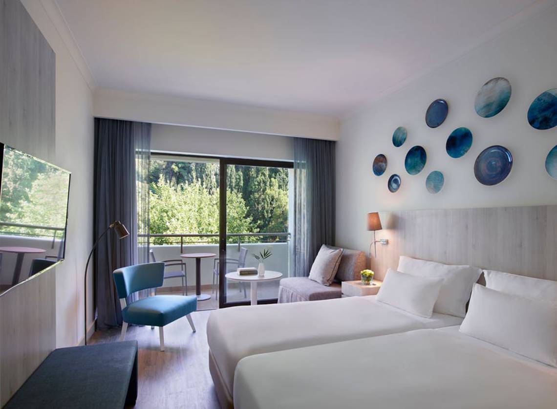 Schlafzimmer im Rhodes Bay Hotel & Spa mit zwei Betten, einem Balkon und modernen Dekorationen.