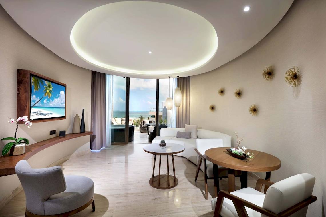 Wohnzimmer des TRS Coral Hotels mit Fernseher, Couch, Tischen und Blick auf das Meer.
