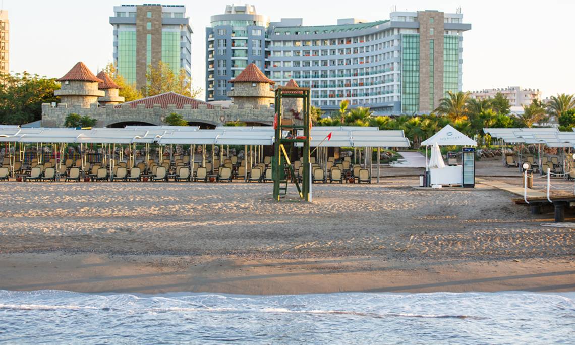 Strand des Sherwood Exclusive Lara Hotels mit Gebäuden im Hintergrund.