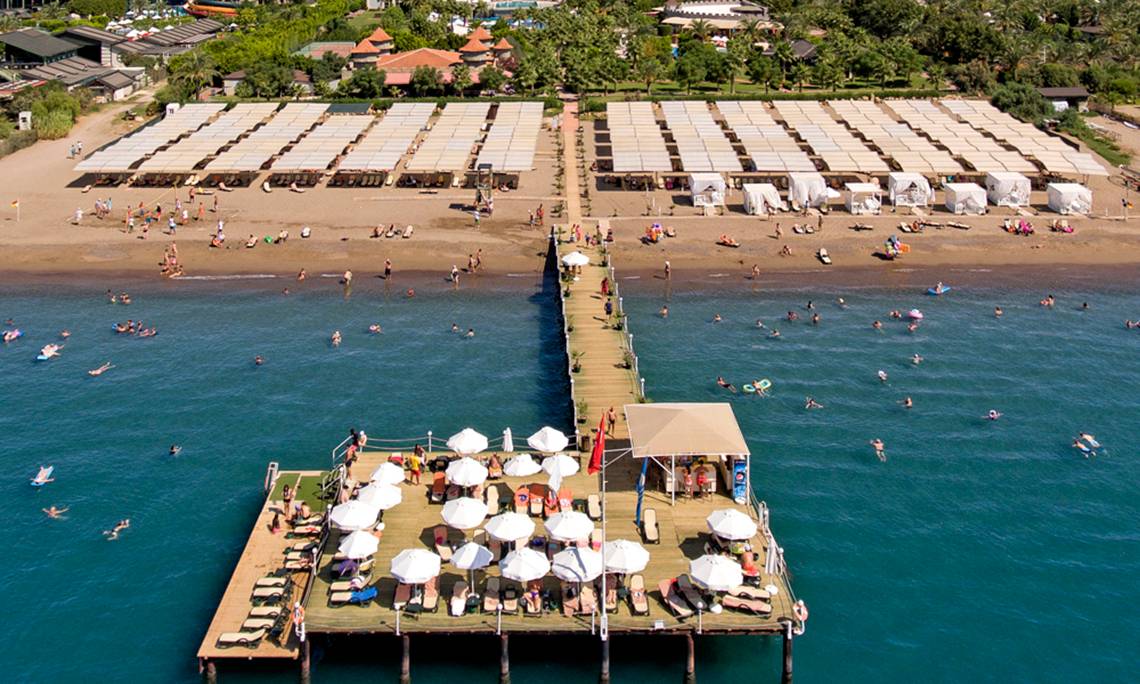 Luftaufnahme des Sherwood Exclusive Lara Hotels mit Strand und vielen Gästen, die schwimmen und sonnenbaden.