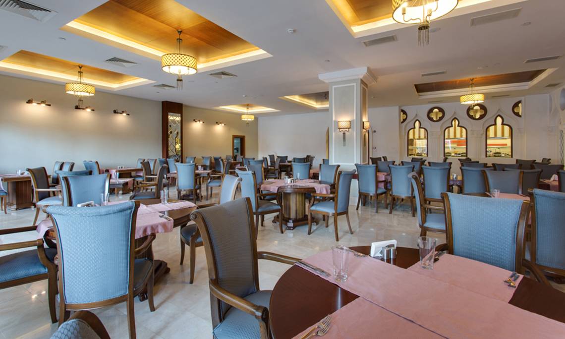 Innenbereich des Restaurants im Sherwood Exclusive Lara Hotel mit blauen Stühlen und Tischen, dekorativ beleuchteten Decken und Wänden.