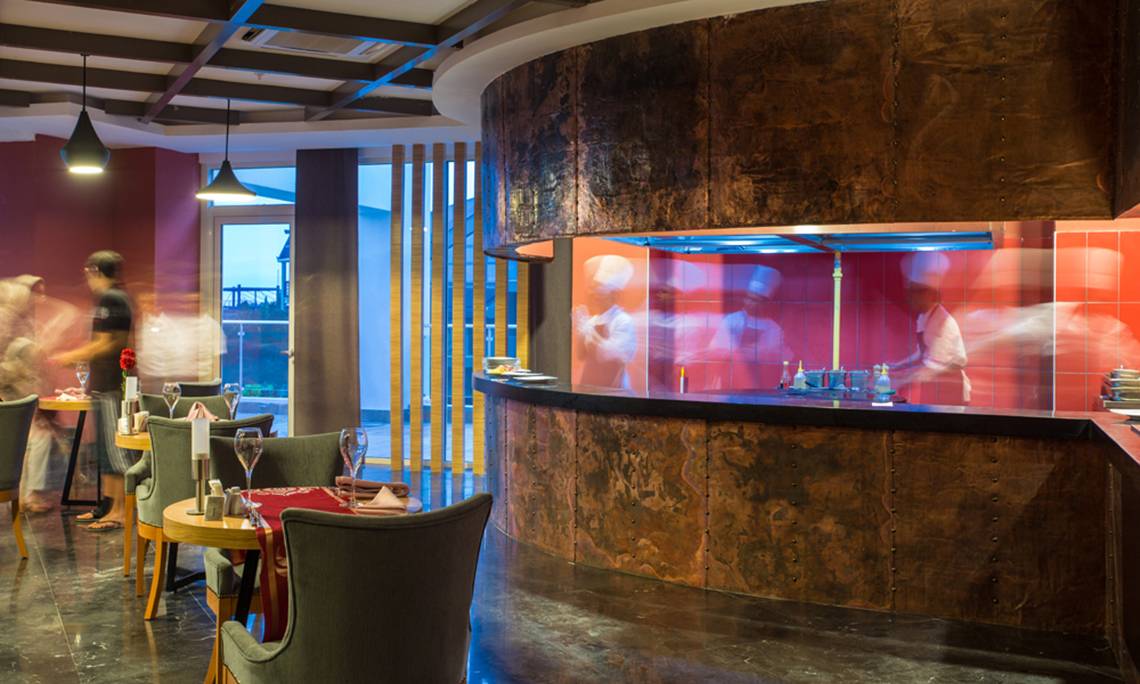 Innenansicht des Restaurants des Sherwood Exclusive Lara Hotels mit einer Theke und rauchenden Personen.