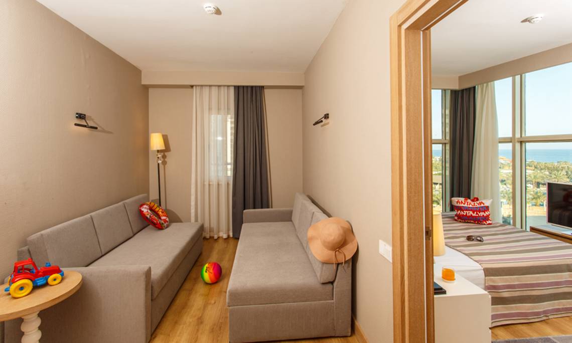 Innenansicht eines Zimmers im Sherwood Exclusive Lara Hotel mit zwei Sofas, einem Tisch, Spielzeug und einem Blick auf das Meer.