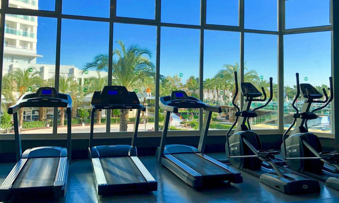 Fitnessstudio mit Laufband und Blick auf Palmen und Gebäude im Sherwood Exclusive Lara