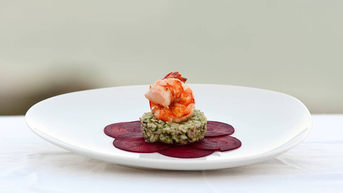 Gegrillter Garnelen-Risotto auf einem weißen Teller mit Rote-Bete-Scheibe.