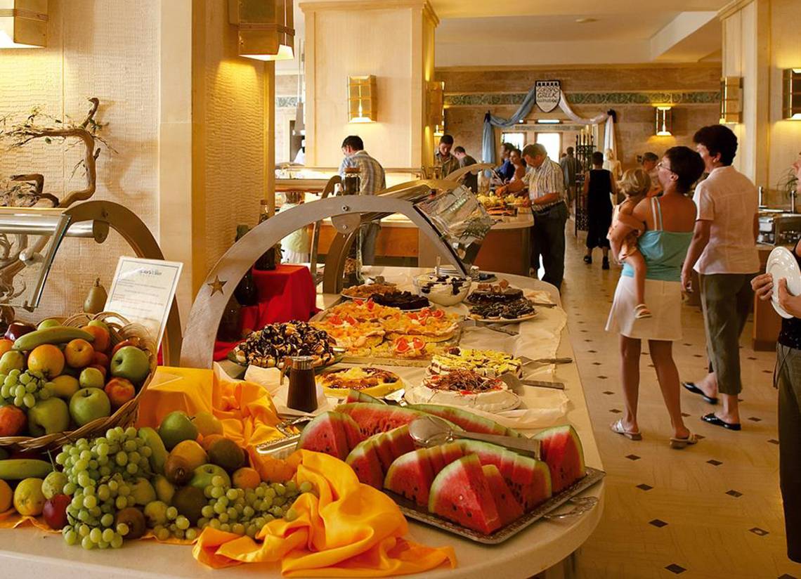 Buffet im Hotel Creta Star mit verschiedenen Desserts, Obst und Menschen, die essen.