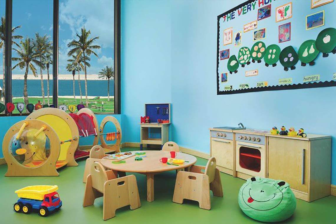 Kinderzimmer im JA Palm Tree Court Hotel mit blauen Wänden, grünem Boden und Spielzeug.