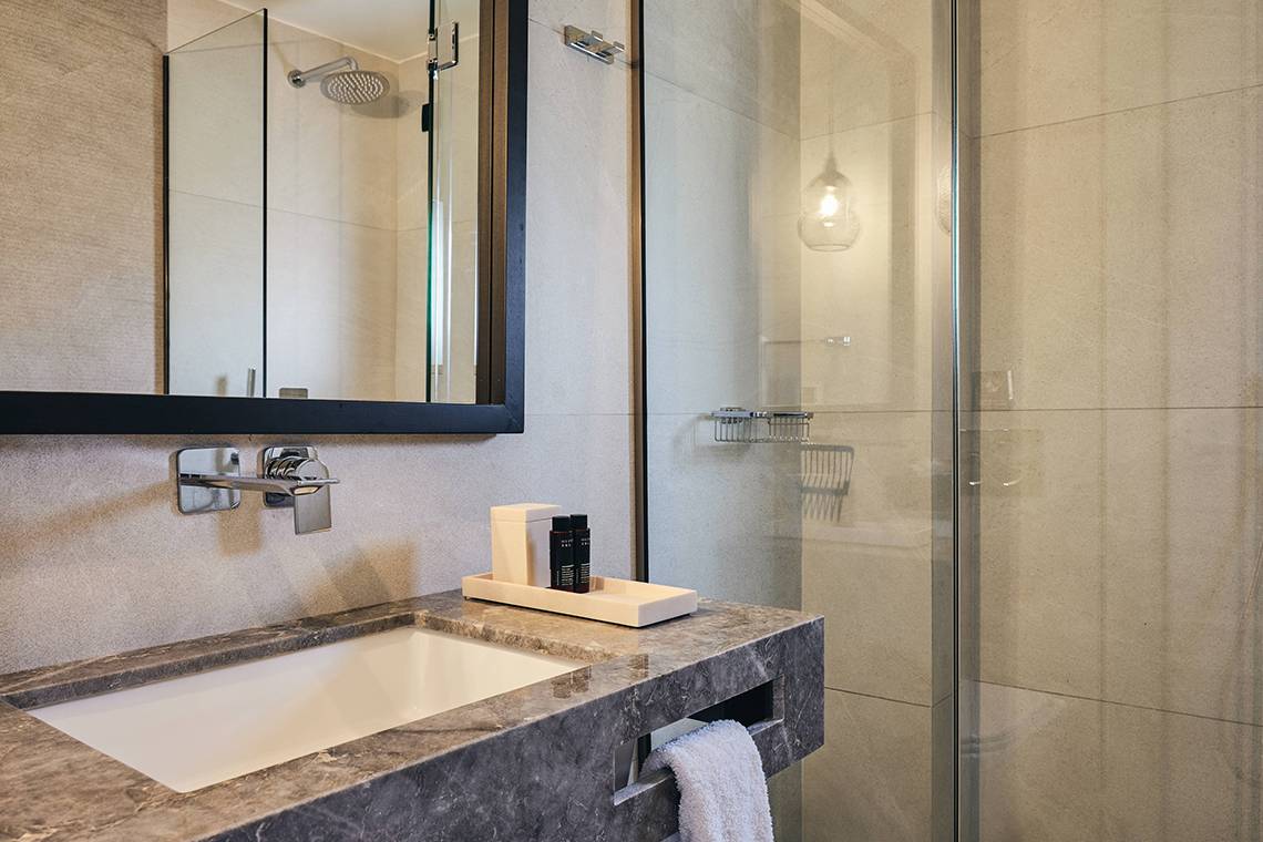 Badezimmer im Domes of Elounda, Autograph Collection mit einer Dusche, Waschbecken und Toilettenartikeln