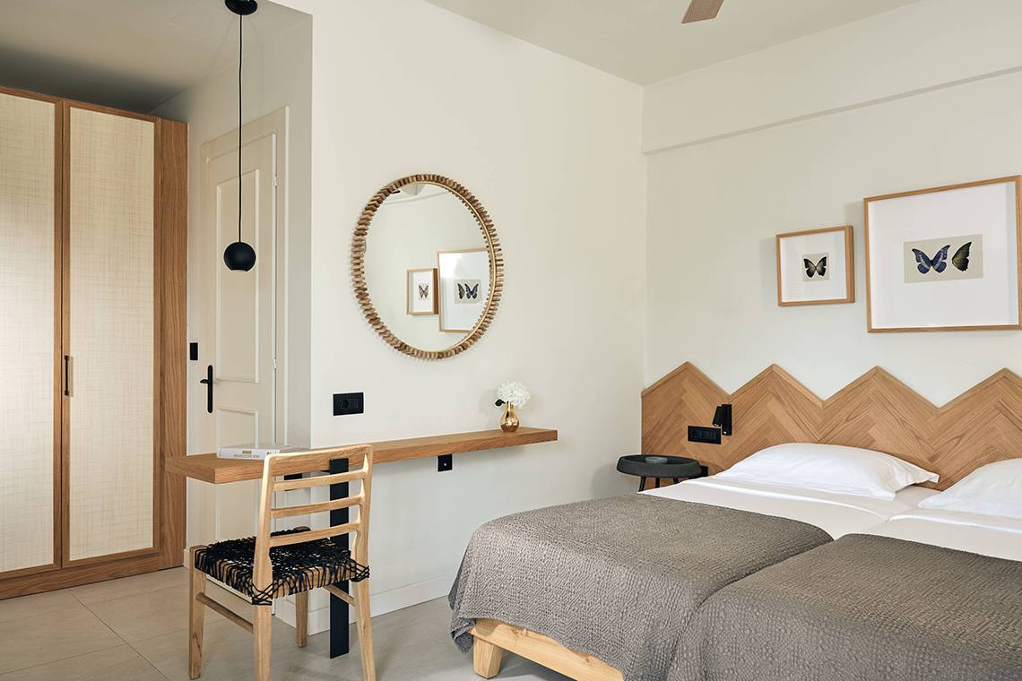 Schlafzimmer mit Doppelbett, Spiegel und Holzmöbeln im Domes of Elounda, Autograph Collection.