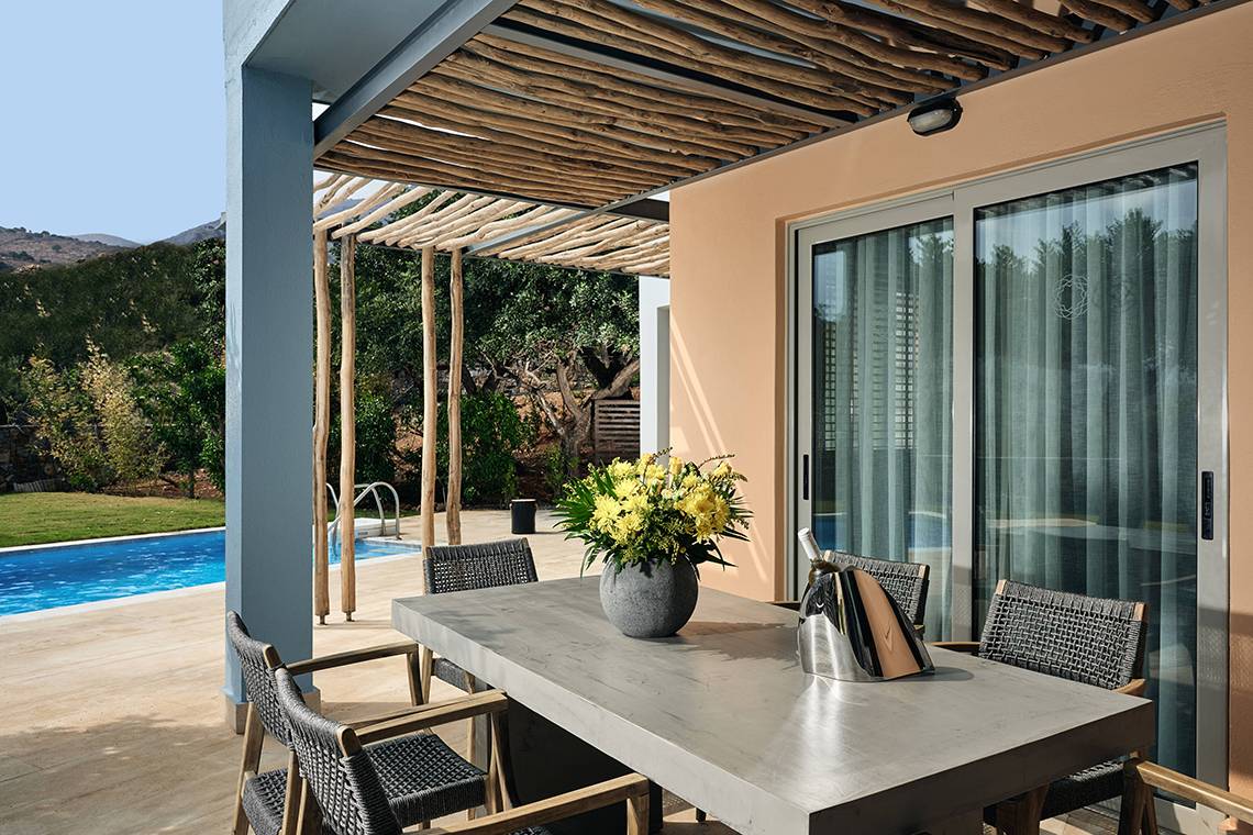 Terrasse im Domes of Elounda, Autograph Collection mit Tisch, Stühlen und Pool im Hintergrund