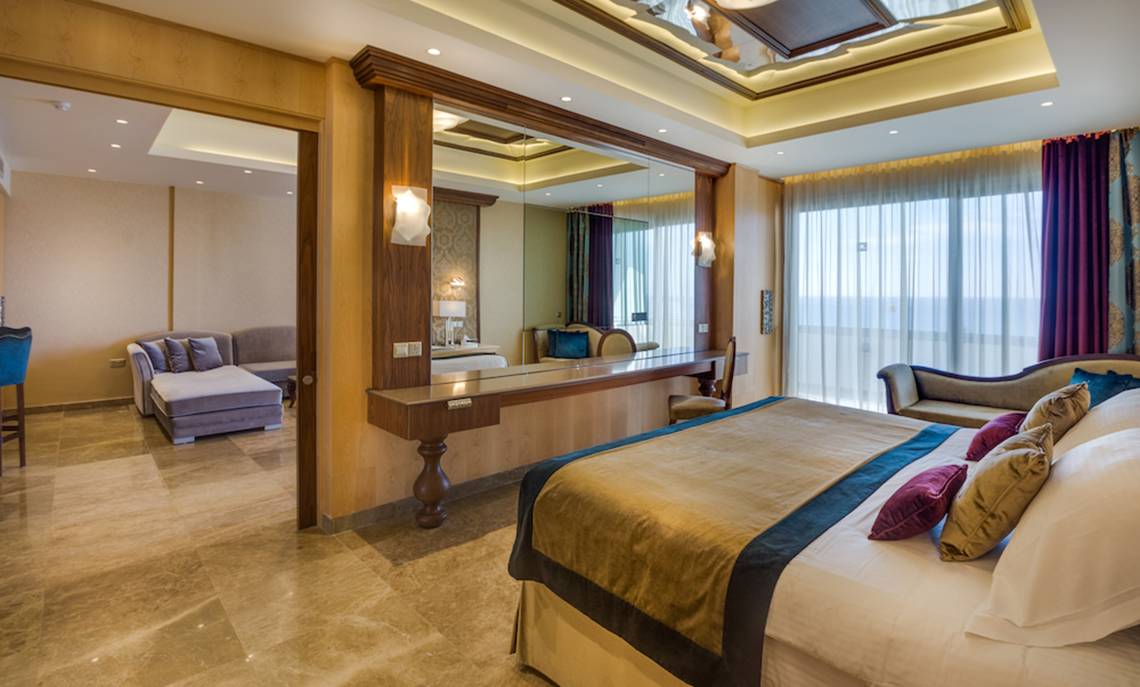 Luxuriöses Schlafzimmer im Adams Beach Hotel mit Doppelbett, Sitzbereich und Spiegel.