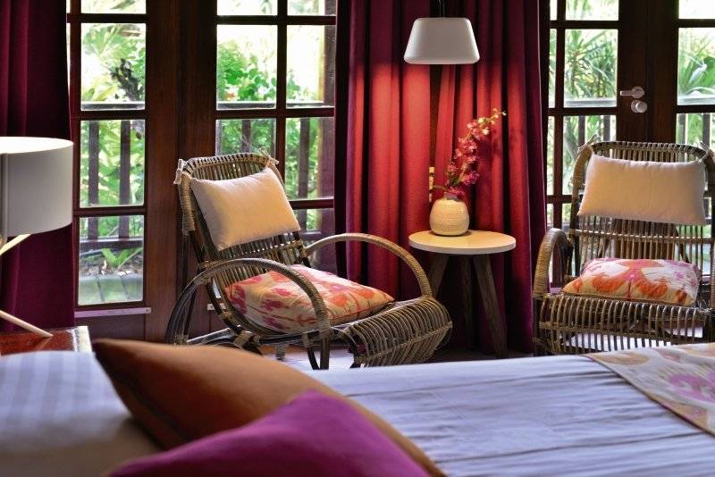Schlafzimmer mit Bett, Sesseln und Blumenvase auf einem kleinen Tisch.