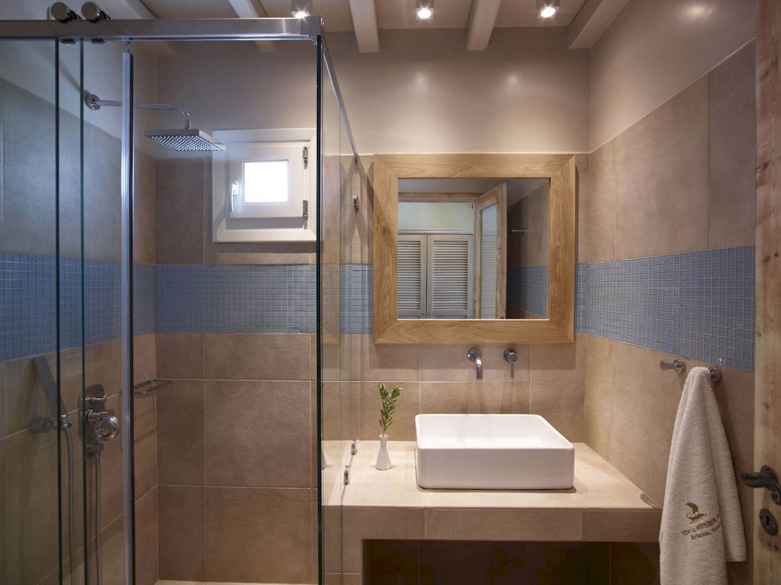 Badezimmer im Vencia Boutique Hotel mit Glasdusche, Waschbecken und beigen Fliesen.