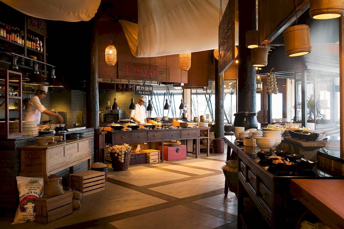 Innenansicht des Restaurants im LUX South Ari Atoll Hotel mit Köchen, die Speisen zubereiten, und vielen Gerichten, die serviert werden.