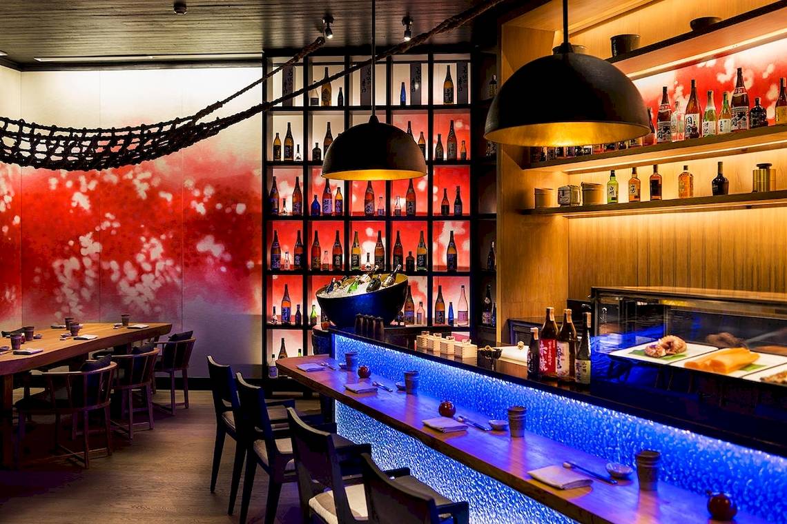Innenansicht des Restaurants im LUX South Ari Atoll Hotel mit roten und weißen Wänden, blau beleuchteten Regalen und Theke.