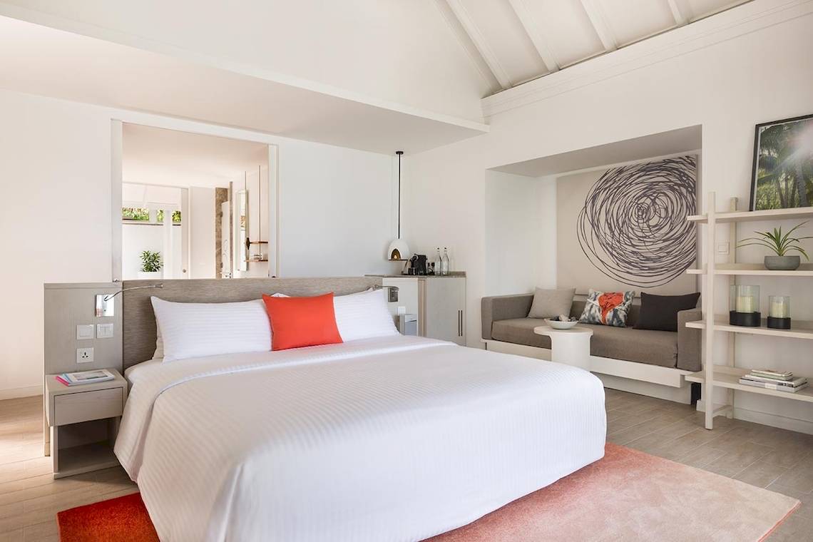 Schlafzimmer im LUX South Ari Atoll mit weißem Bett, rotem Kissen und moderner Einrichtung.